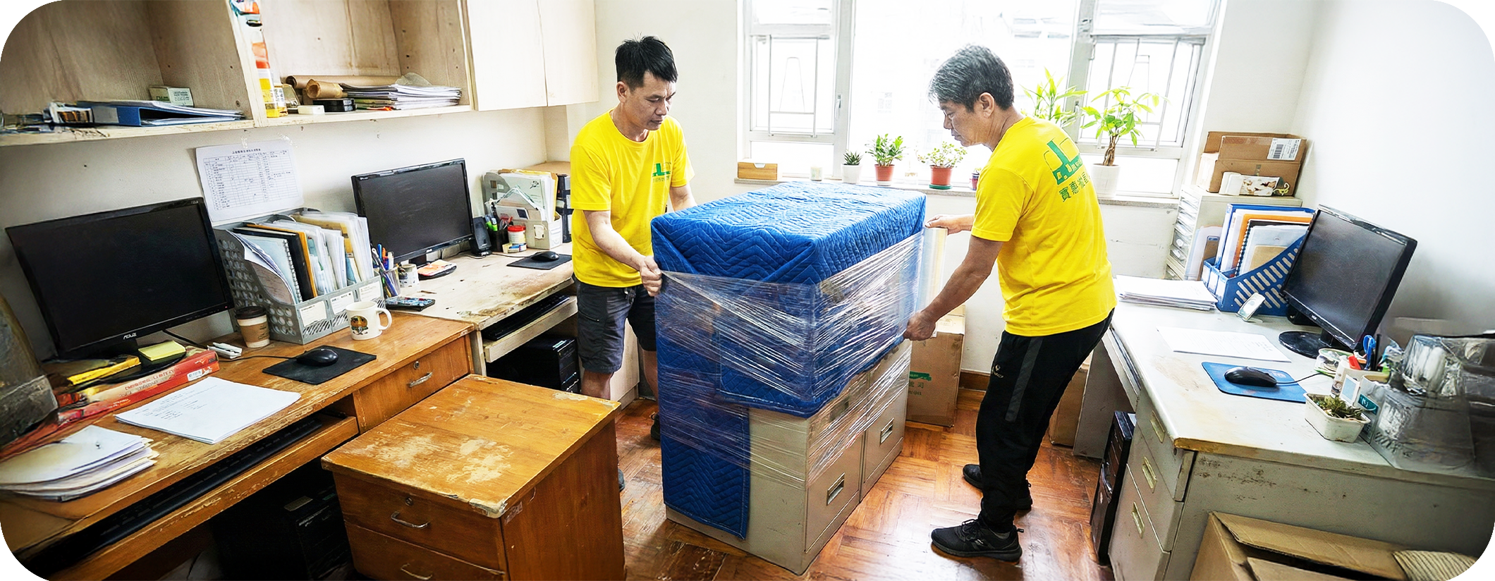 實惠搬屋專業團隊在寫字樓內合力使用拉伸膜為大型文件櫃進行防護包裝，展示針對辦公室搬運及公司搬遷的文件安全與傢俬保護措施。是香港企業信賴的寫字樓搬屋公司推介。
