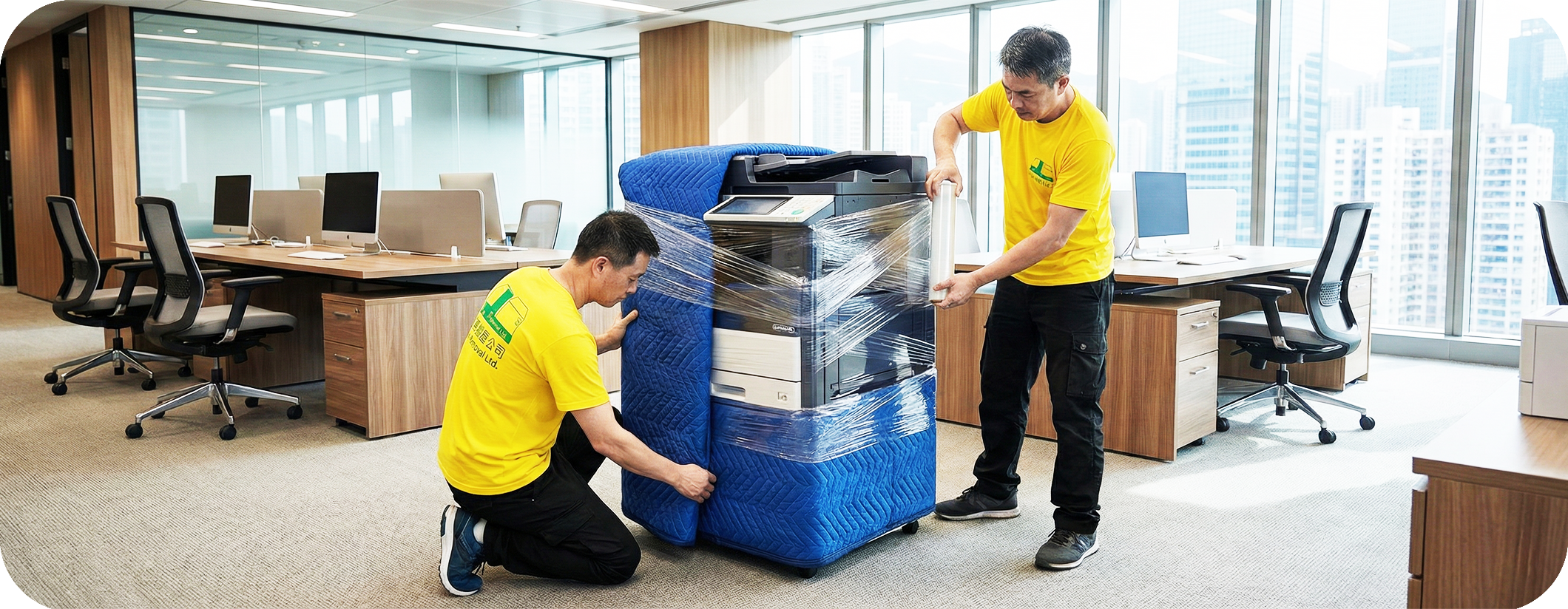 實惠搬屋兩位專業師傅在現代化辦公室內，使用藍色加厚保護毯及膠膜嚴密包裹大型商用影印機。展示針對貴重儀器、伺服器及電子設備的專業寫字樓搬運技術，確保零損壞。