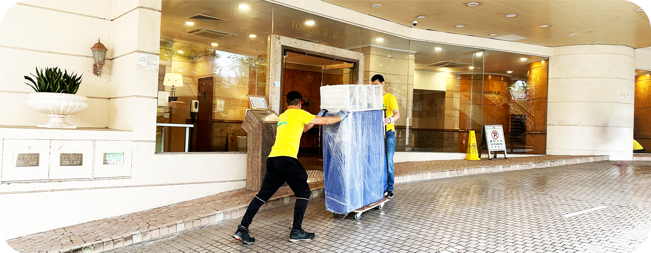 兩名實惠搬屋搬運人員合作將大型雪櫃經由屋苑大堂斜路安全運送至貨車位置。