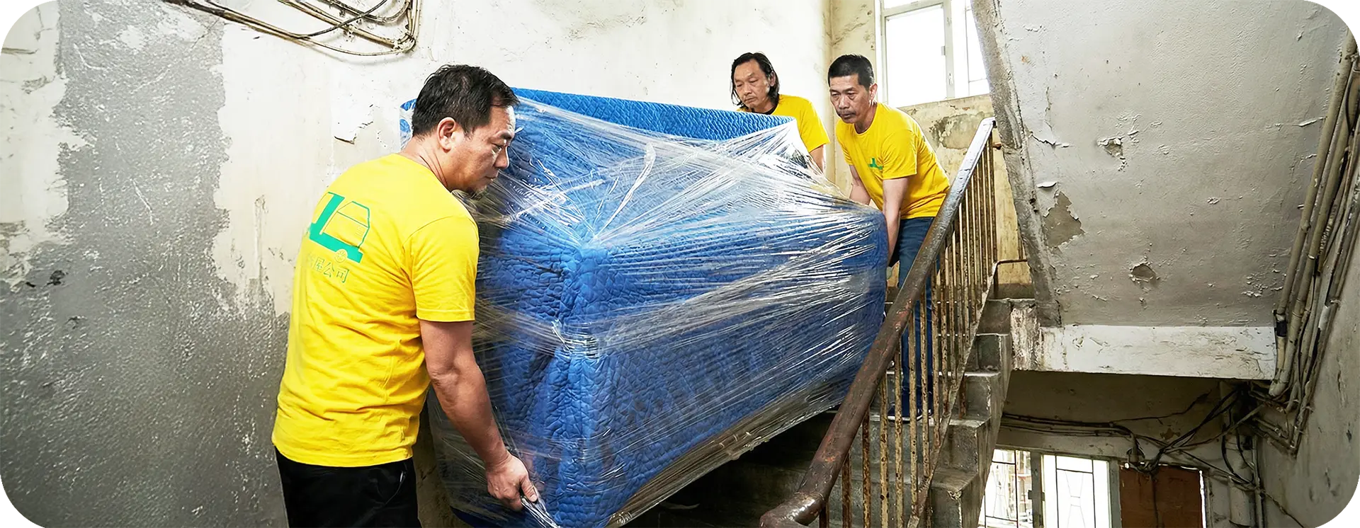 實惠搬屋公司三名專業搬運師傅在狹窄樓梯間合力搬運經嚴密保護包裝的鋼琴。展示針對唐樓及無電梯大廈的高難度搬運服務，體現專業搬屋公司在重物搬運與團隊協作上的頂尖技術。